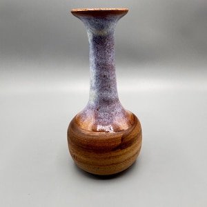 Puede incluir: Un jarrón de cerámica con base redonda y cuello estrecho. El jarrón está esmaltado en tonos marrones, morados y blancos.