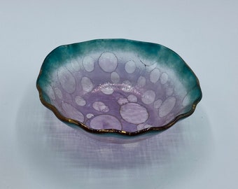 May include: A small, scalloped glass bowl with a purple and teal iridescent finish. The bowl has a gold rim and is decorated with a pattern of white circles.