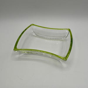 May include: A clear glass dish with a lime green rim. The dish is slightly curved and has a rectangular shape.