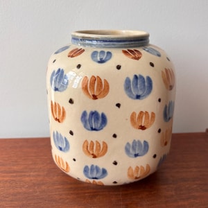May include: A white ceramic vase with a blue and orange floral pattern. The vase has a rounded body and a slightly flared lip.