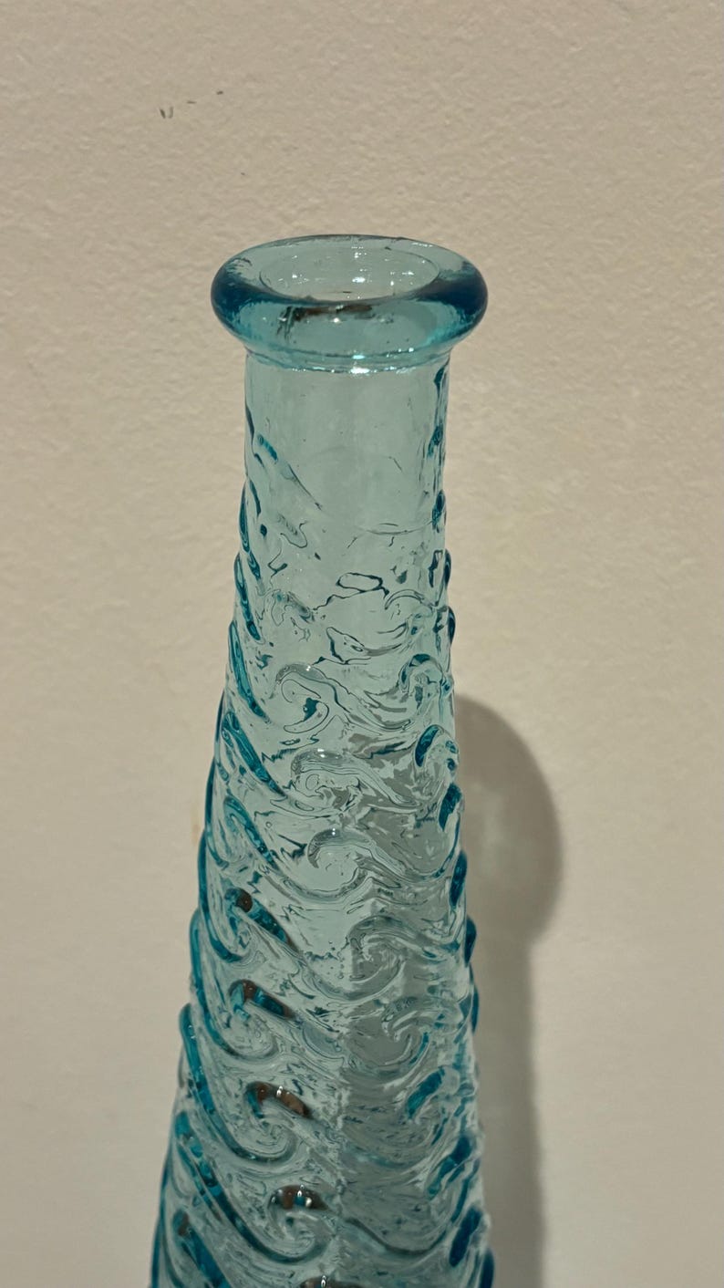 May include: A tall, clear blue glass vase with a wavy, textured design.