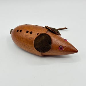 May include: A wooden mouse pincushion with red jewel eyes and brown suede ears. The mouse is carved from wood and has a series of holes for needles.