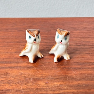 Peut inclure: Deux petites figurines de hiboux en céramique. Les hiboux ont des corps blancs, des ailes et des marques de tête marron, des yeux bleus et des becs rouges. Ils sont posés sur une surface en bois.