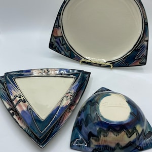 Puede incluir: Conjunto de tres platos de cerámica triangulares con un diseño abstracto en azul, verde y rosa. Los platos están apilados uno encima del otro. El plato más grande es un plato para cenar, el plato del medio es un plato para ensalada y el plato más pequeño es un plato para postre.