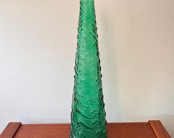 May include: A tall, green glass vase with a textured, wave-like pattern. The vase has a slender, conical shape and stands on a wooden surface. The vase is approximately 14 inches tall.
