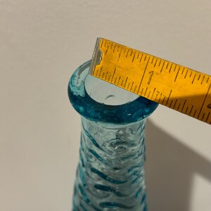 May include: A turquoise blue glass vase with a textured surface. The vase is approximately 1 inch in diameter at the opening.