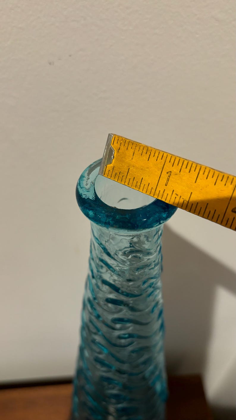 May include: A turquoise blue glass vase with a textured surface. The vase is approximately 1 inch in diameter at the opening.