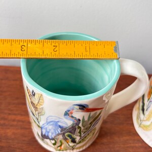 Puede incluir: Taza de cer&aacute;mica blanca con un dise&ntilde;o de garza azul. El interior y el borde son de color turquesa. La taza tiene aproximadamente 7,6 cm de di&aacute;metro, medido con una regla. El asa es blanca y curvada.