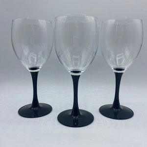 May include: Set of three clear glass wine glasses with black stems and bases.