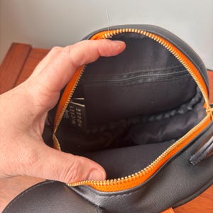 May include: Black backpack with orange zipper and trim. The interior is black with a small zippered pocket. The backpack has a gold zipper and the words "MICKEY HOUSE" are visible on a tag inside the bag.