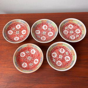 May include: Five small, round, red and white ceramic dishes with intricate Chinese designs. Each dish features a central floral pattern and Chinese characters, surrounded by a decorative border with blue, green, and gold accents.