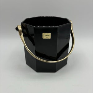 May include: A black octagonal ice bucket with a glossy finish and a gold-toned metal swing handle. A rectangular sticker on the front features the text Luminarc Verrerie d'Arques France. The bucket has a wide opening and a flat base.
