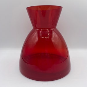 Peut inclure: Un vase en verre rouge avec une base large et un col étroit. Le vase est en verre clair avec une teinte rouge.