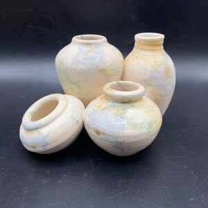 Puede incluir: Cuatro jarrones de cerámica de diferentes tamaños, cada uno con un esmalte blanco y sutiles matices azules y verdes. Los jarrones están dispuestos sobre una superficie negra.