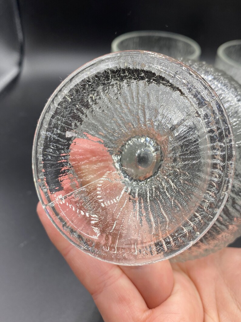 May include: Close-up of the bottom of a clear glass drinking glass with a textured, rippled design.