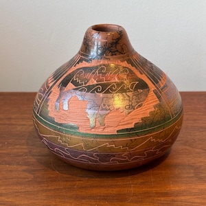 May include: A round terracotta vase featuring a carved buffalo silhouette on the front. The surface displays a dark horsehair-style crackle pattern, horizontal bands of green and purple, and etched geometric lines throughout the exterior.