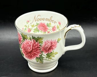 May include: White ceramic mug with a gold rim and floral design. The mug has the word "November" written on the side in gold lettering.