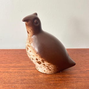 Könnte beinhalten: Braune Keramik-Vogelfigur mit einem gesprenkelten Muster auf der unteren Hälfte. Der Vogel hat einen glatten, abgerundeten Körper und einen kleinen, spitzen Schnabel. Die Figur ist ein dekorativer Gegenstand, wahrscheinlich zur Dekoration.