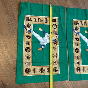 May include: Two green pillowcases with a baseball player in a white uniform throwing a ball. The pillowcases have a tan border with logos of different baseball teams.