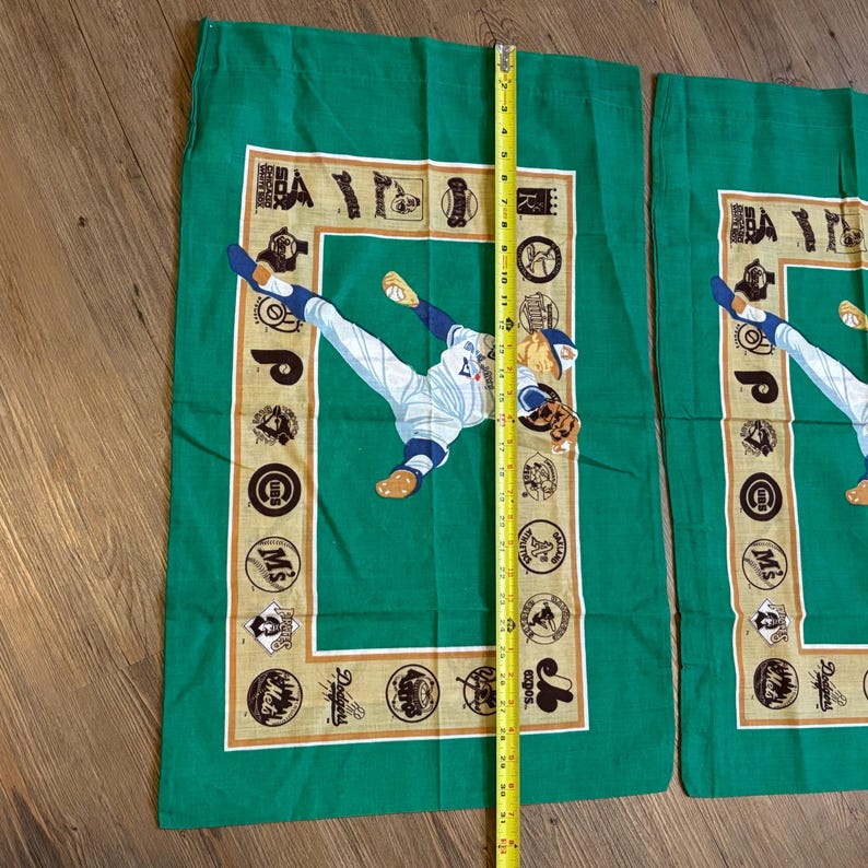 May include: Two green pillowcases with a baseball player in a white uniform throwing a ball. The pillowcases have a tan border with logos of different baseball teams.
