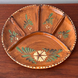 May include: Brown ceramic serving platter with five sections. The platter is decorated with green and white floral designs and a dotted border. The sections are separated by raised dividers. A decorative piece for serving snacks or appetizers.
