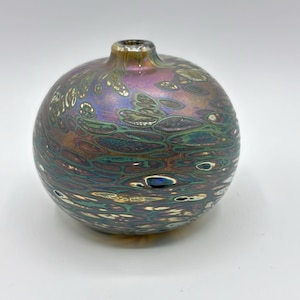Peut inclure: Un petit vase rond en verre iridescent avec un motif tourbillonnant de brun, vert et or. Le vase a une ouverture étroite en haut.