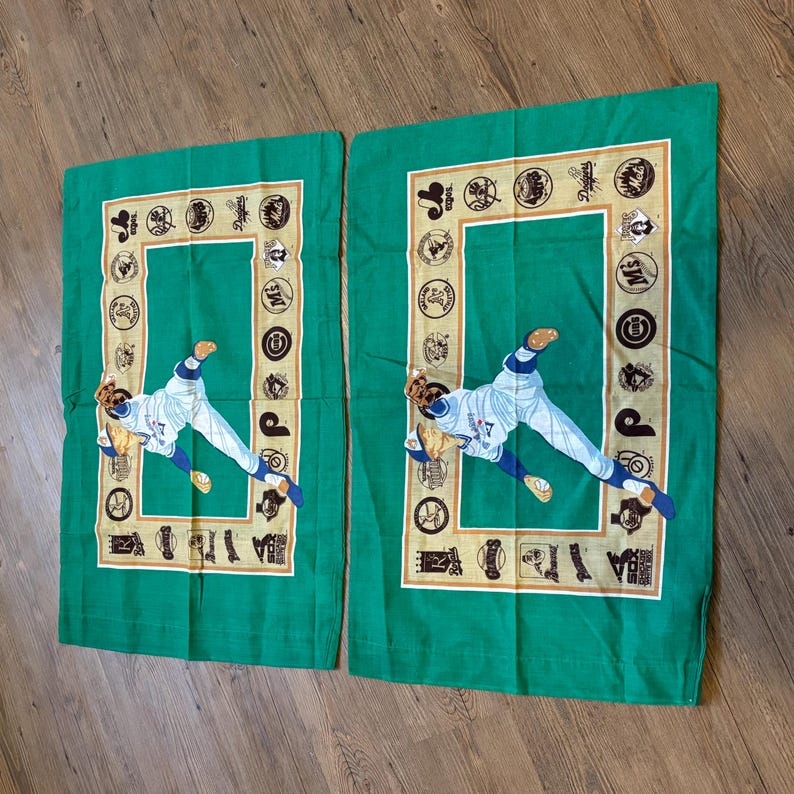 May include: Two green pillowcases with a baseball player in a white uniform throwing a ball. The pillowcases have a gold border with baseball team logos around the edge.