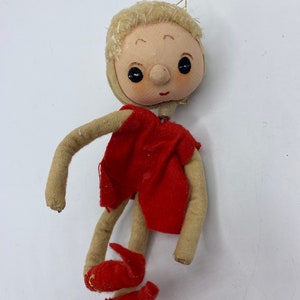 Könnte beinhalten: Eine handgemachte Vintage-Puppe mit blonden Haaren, einem roten Kleid und roten Schuhen. Die Puppe hat ein süßes, lächelndes Gesicht und ist aus Stoff gefertigt.