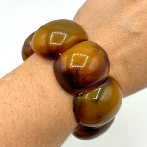 May include: A brown and amber chunky resin bracelet with a glossy finish. The bracelet is made of large, rounded beads.