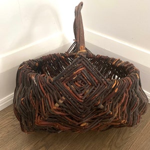 May include: A woven basket made of brown twigs with a unique diamond pattern. The basket has a single handle and is ideal for storage or display.