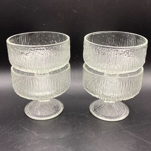 May include: Set of four clear glass dessert bowls with a textured, frosted finish. Each bowl has a pedestal base.