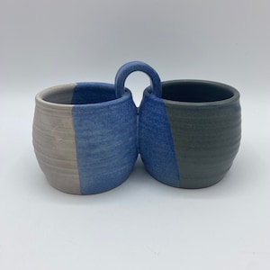 May include: A ceramic serving dish with two connected bowls. The bowls are painted in shades of blue, gray, and white.