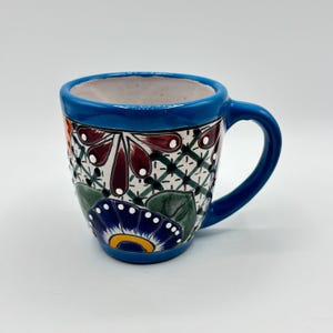 May include: A blue ceramic mug with a colourful floral design. The mug has a white background with red, green, blue, yellow, and orange flowers.
