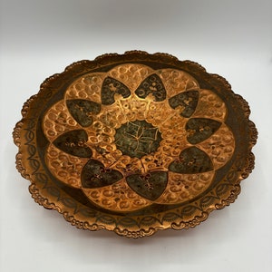 May include: A round, decorative brass tray with a scalloped edge. The tray features an intricate design of gold and green swirls and patterns.