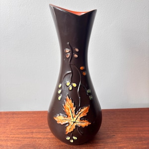 May include: A brown ceramic vase with an orange interior. The vase features a detailed design of a maple leaf and vines with yellow and orange accents. The vase is approximately 10 inches tall.