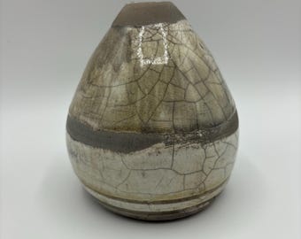 May include: A small, pear-shaped ceramic vase with a crackled glaze in shades of brown, white, and grey. The vase has a textured surface and a slightly uneven rim.