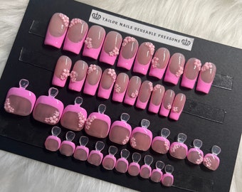 May include: A set of 24 pink reusable press-on nails with a floral design. The nails are arranged in rows on a black display card with the text "TAILOR NAILS REUSABLE PRESSONS".
