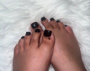 May include: Close-up of two bare feet with black square-shaped nail polish on the toes.