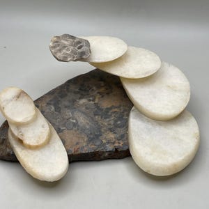 Peut inclure: Sculpture abstraite en pierre. Une base sombre et textur&eacute;e soutient des pierres ovales blanches, avec une petite pierre grise textur&eacute;e au sommet. L'arrangement cr&eacute;e un design artistique &eacute;quilibr&eacute;. Sculpture en pierre naturelle.