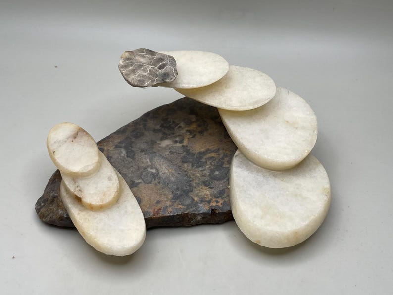 Peut inclure: Sculpture abstraite en pierre. Une base sombre et textur&eacute;e soutient des pierres ovales blanches, avec une petite pierre grise textur&eacute;e au sommet. L'arrangement cr&eacute;e un design artistique &eacute;quilibr&eacute;. Sculpture en pierre naturelle.