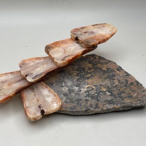 Peut inclure: Une sculpture en pierre naturelle compos&eacute;e de morceaux rectangulaires superpos&eacute;s de pierre dans des tons de beige, marron et blanc, &eacute;quilibr&eacute;s sur une base de pierre plate, sombre et textur&eacute;e. L'arrangement cr&eacute;e un design abstrait unique.