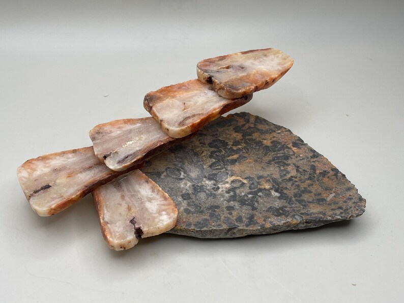 Peut inclure: Une sculpture en pierre naturelle compos&eacute;e de morceaux rectangulaires superpos&eacute;s de pierre dans des tons de beige, marron et blanc, &eacute;quilibr&eacute;s sur une base de pierre plate, sombre et textur&eacute;e. L'arrangement cr&eacute;e un design abstrait unique.