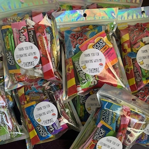 Pu&ograve; includere: Diversi sacchetti di plastica trasparenti pieni di caramelle colorate e piccoli giocattoli. Ogni sacchetto ha un adesivo rotondo con un personaggio dei cartoni animati e il testo "Grazie per aver festeggiato con me! -Thomas".
