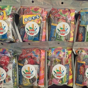 Pu&ograve; includere: Sei sacchetti di plastica trasparenti pieni di varie caramelle colorate, ogni sacchetto ha un adesivo rotondo con il testo "Quest'anno &egrave; stato cos&igrave; dolce!" e un disegno di una matita, un righello e una mela.
