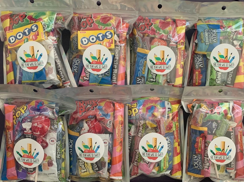 Pu&ograve; includere: Sei sacchetti di plastica trasparenti pieni di varie caramelle colorate, ogni sacchetto ha un adesivo rotondo con il testo "Quest'anno &egrave; stato cos&igrave; dolce!" e un disegno di una matita, un righello e una mela.