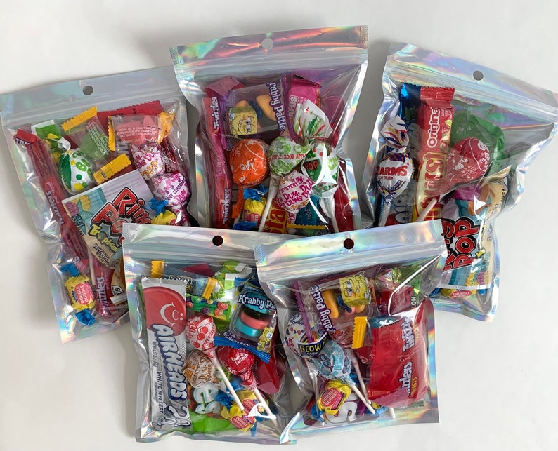 Pu&ograve; includere: Quattro sacchetti di plastica trasparenti pieni di varie caramelle colorate, tra cui lecca-lecca, caramelle gommose e cioccolato. I sacchetti sono iridescenti e hanno una chiusura a zip.