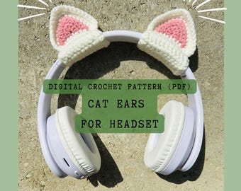 May include: White crochet cat ears for a headset. The ears are pink on the inside and white on the outside. The text "DIGITAL CROCHET PATTERN (PDF) CAT EARS FOR HEADSET" is on the image.