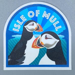 May include: A blue and white sticker with the text "Isle of Mull" in white letters. Two cartoon puffins are facing each other in the center of the sticker. The puffins are white with black backs and orange beaks. The background is a blue and white striped pattern.