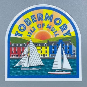 May include: A yellow and blue sticker with the text "Tobermory Isle of Mull" in a white circle with a stylized sun rising behind it. The sticker features two sailboats on a blue body of water with a row of colorful houses in the background.