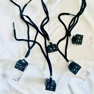 May include: Five black car air fresheners with black string hangers. Each air freshener has a clear glass bottle with a black decorative top.